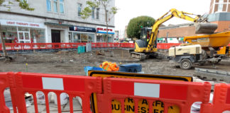 A sign saying businesses open as usual obscured by a roadworks barrier.